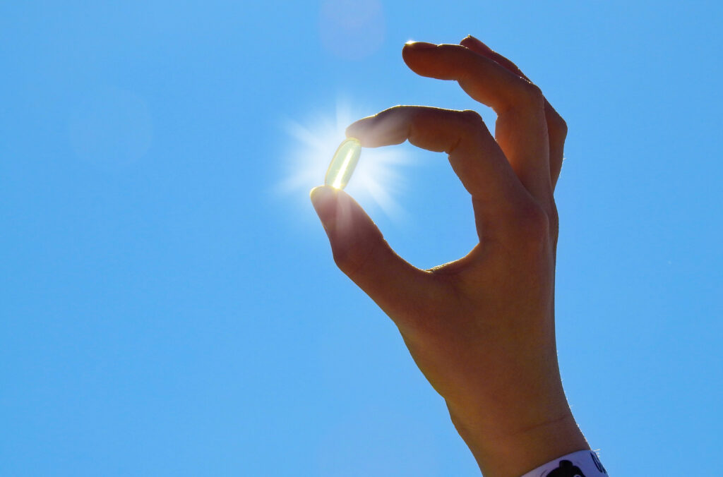 Hand holding a Vitamin D pill with the sun shining in the background.